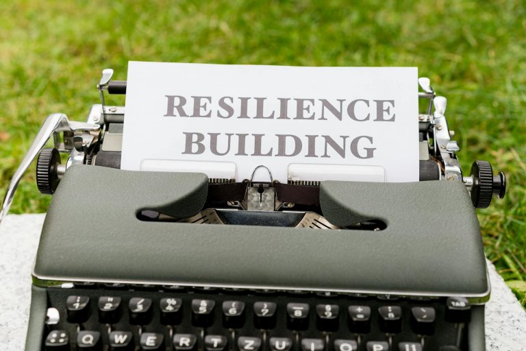 Vintage typewriter with 'Resilience Building' text on paper, set outdoors on grass.